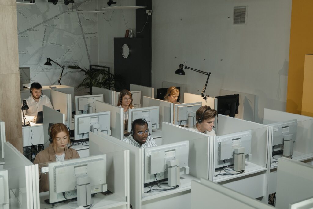 Immagine di un ufficio bianco con sei persone al lavoro su un software per call center, mentre tre postazioni di lavoro sono vuote